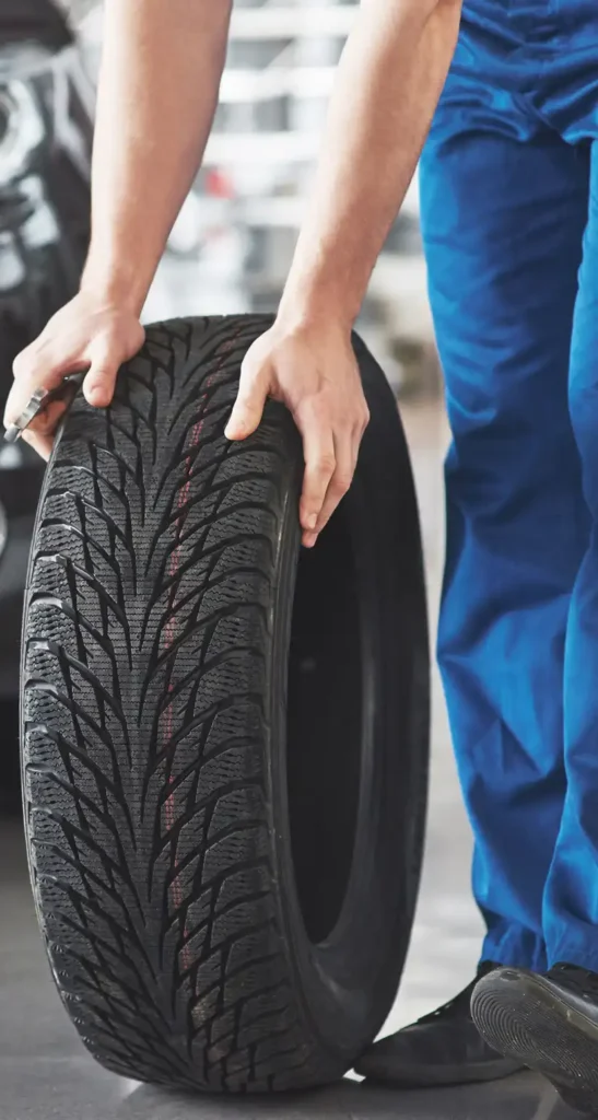 Monteur die een band positioneert voor installatie in een autoservicecentrum, ter voorbereiding op seizoensgebonden rijomstandigheden.